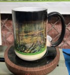 A Magic decorative coffee mug featuring a scenic landscape design, placed on a wooden coaster.