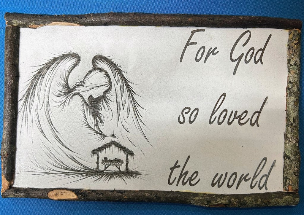 A decorative wooden sign featuring an angel design and the text 'For God so loved the world'.