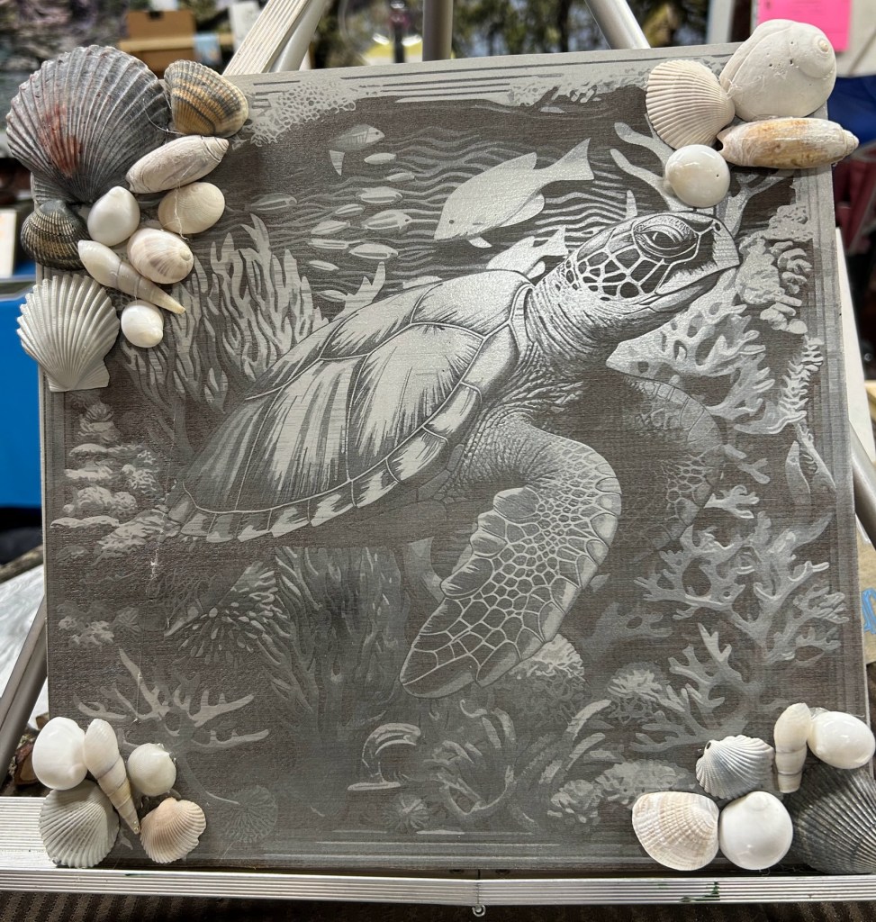 A decorative piece featuring an engraved sea turtle surrounded by various seashells, set against a textured background depicting underwater scenery.