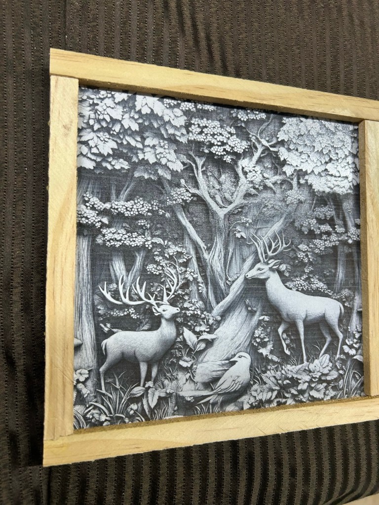 A black and white illustration of deer and a bird amidst a forest scene, framed in a light wooden border.
